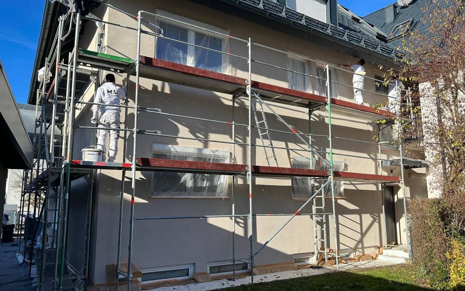 Drei MEL-Mitarbeiter streichen eine Hausfassade vom Gerüst aus