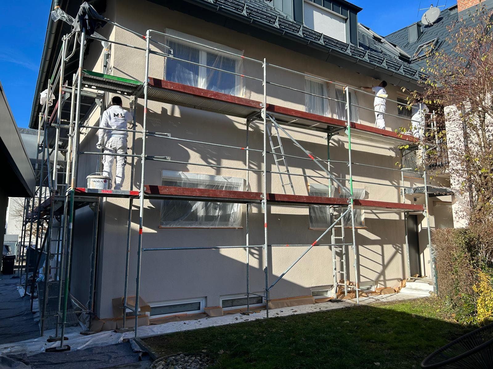 Drei MEL-Mitarbeiter streichen eine Fassade vom Gerüst