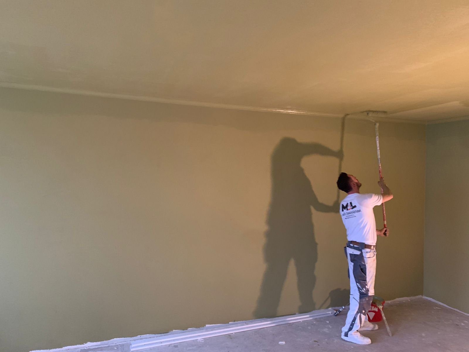 MEL-Maler streicht eine Decke über salbeifarbener Wand